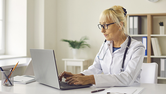 clinician-in-office-typing-on-laptop-measuring-epidermal-effects-of-ostomy-skin-barriers-575x325